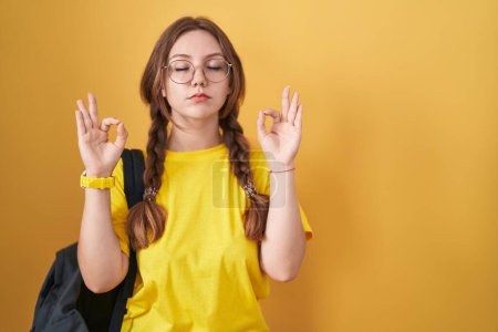 Photo for Young caucasian woman wearing student backpack over yellow background relaxed and smiling with eyes closed doing meditation gesture with fingers. yoga concept. - Royalty Free Image