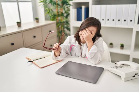 Photo for Down syndrome woman wearing doctor uniform stressed working at clinic - Royalty Free Image