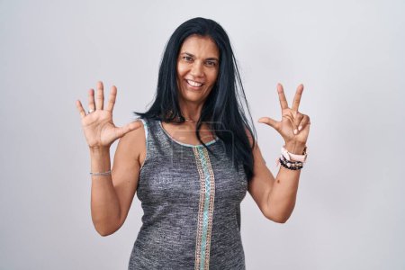 Photo for Mature hispanic woman standing over white background showing and pointing up with fingers number eight while smiling confident and happy. - Royalty Free Image