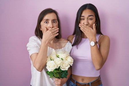 Photo for Hispanic mother and daughter holding bouquet of white flowers shocked covering mouth with hands for mistake. secret concept. - Royalty Free Image