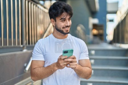 Photo for Young hispanic man smiling confident using smartphone at street - Royalty Free Image