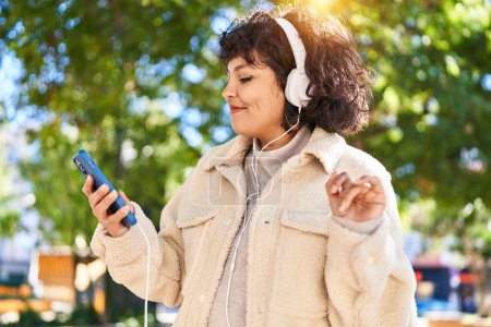 Téléchargez les photos : Jeune belle femme hispanique souriant confiant écouter de la musique au parc - en image libre de droit