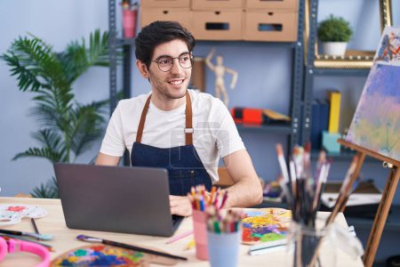 Téléchargez les photos : Young hispanic man artist smiling confident using laptop at art studio - en image libre de droit