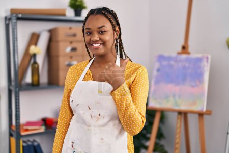 Foto de Mujer afroamericana con trenzas en el estudio de arte sonriendo feliz y positivo, pulgar hacia arriba haciendo excelente y signo de aprobación - Imagen libre de derechos