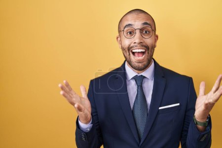 Photo for Hispanic man with beard wearing suit and tie celebrating crazy and amazed for success with arms raised and open eyes screaming excited. winner concept - Royalty Free Image