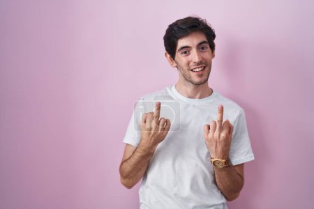 Foto de Young hispanic man standing over pink background showing middle finger doing fuck you bad expression, provocation and rude attitude. screaming excited - Imagen libre de derechos