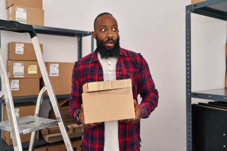Téléchargez les photos : Afro-Américain travaillant dans une petite entreprise e-commerce dans le visage de choc, l'air sceptique et sarcastique, surpris avec la bouche ouverte - en image libre de droit