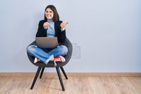 Photo for Young hispanic woman sitting on chair using computer laptop pointing to the back behind with hand and thumbs up, smiling confident - Royalty Free Image