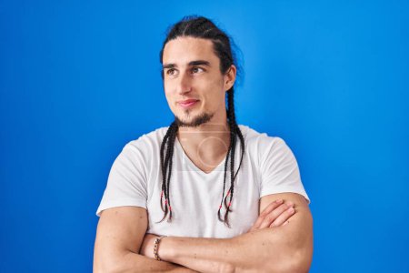 Photo for Hispanic man with long hair standing over blue background smiling looking to the side and staring away thinking. - Royalty Free Image