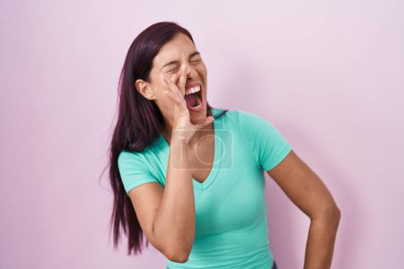 Téléchargez les photos : Young hispanic woman standing over pink background shouting and screaming loud to side with hand on mouth. communication concept. - en image libre de droit