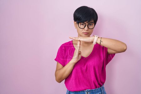 Téléchargez les photos : Jeune femme asiatique avec les cheveux courts debout sur fond rose faisant le temps geste avec les mains, frustré et sérieux visage - en image libre de droit