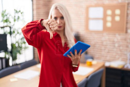 Photo for Caucasian woman working at the office with tablet looking unhappy and angry showing rejection and negative with thumbs down gesture. bad expression. - Royalty Free Image