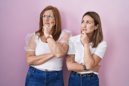 Photo for Hispanic mother and daughter wearing casual white t shirt over pink background thinking worried about a question, concerned and nervous with hand on chin - Royalty Free Image