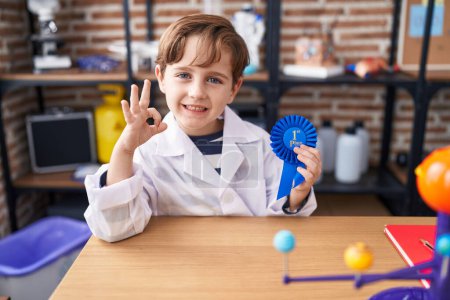 Téléchargez les photos : Petit garçon caucasien au laboratoire scientifique de l'école remportant le premier prix faisant ok signe avec les doigts, sourire geste amical excellent symbole - en image libre de droit