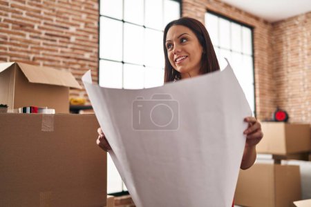 Photo for Young beautiful hispanic woman smiling confident reading house plans at new home - Royalty Free Image