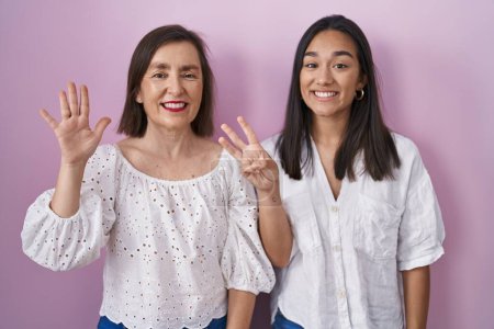 Téléchargez les photos : Mère hispanique et fille ensemble montrant et pointant vers le haut avec les doigts numéro huit tout en souriant confiant et heureux. - en image libre de droit
