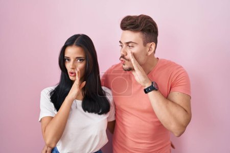 Téléchargez les photos : Jeune couple hispanique debout sur fond rose main sur bouche racontant rumeur secrète, chuchotant conversation malicieuse - en image libre de droit