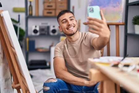 Photo for Young hispanic man artist making selfie by the smartphone at art studio - Royalty Free Image