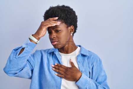 Téléchargez les photos : Femme afro-américaine debout sur fond bleu touchant le front pour la maladie et la fièvre, la grippe et le rhume, le virus malade - en image libre de droit