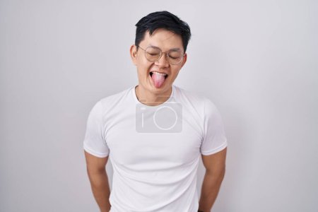 Téléchargez les photos : Jeune homme asiatique debout sur fond blanc langue collante heureux avec une expression drôle. concept d'émotion. - en image libre de droit