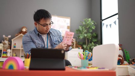 Téléchargez les photos : Young chinese man preschool teacher having online vocabulary lesson at kindergarten - en image libre de droit