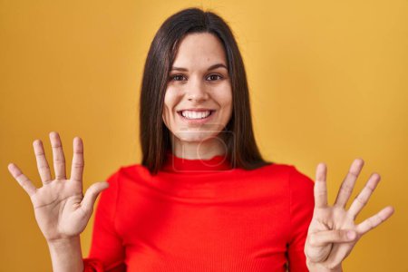 Photo for Young hispanic woman standing over yellow background showing and pointing up with fingers number nine while smiling confident and happy. - Royalty Free Image