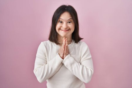 Photo for Woman with down syndrome standing over pink background praying with hands together asking for forgiveness smiling confident. - Royalty Free Image