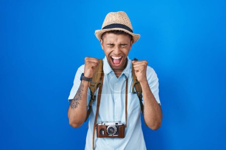 Foto de Joven brasileño sosteniendo cámara vintage emocionado por el éxito con los brazos levantados y los ojos cerrados celebrando la victoria sonriendo. concepto ganador. - Imagen libre de derechos
