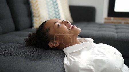 Téléchargez les photos : Femme afro-américaine détendue avec la tête sur le canapé assis sur le sol à la maison - en image libre de droit