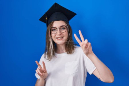 Photo for Blonde caucasian woman wearing graduation cap smiling looking to the camera showing fingers doing victory sign. number two. - Royalty Free Image