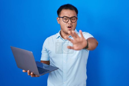 Téléchargez les photos : Jeune homme chinois utilisant un ordinateur portable faisant geste d'arrêt avec les mains paumes de la main, expression de colère et de frustration - en image libre de droit
