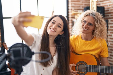 Téléchargez les photos : Deux femmes musiciens jouant de la guitare classique faisant selfie par smartphone au studio de musique - en image libre de droit