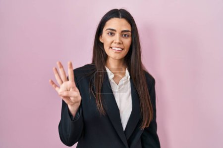 Téléchargez les photos : Jeune femme brune portant un style d'affaires sur fond rose montrant et pointant vers le haut avec les doigts numéro quatre tout en souriant confiant et heureux. - en image libre de droit