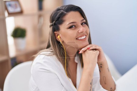 Photo for Young hispanic woman listening to music sitting on table at home - Royalty Free Image