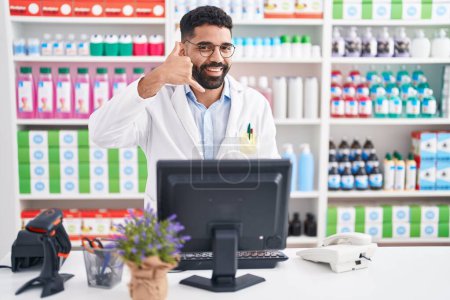 Photo for Hispanic man with beard working at pharmacy drugstore smiling doing phone gesture with hand and fingers like talking on the telephone. communicating concepts. - Royalty Free Image