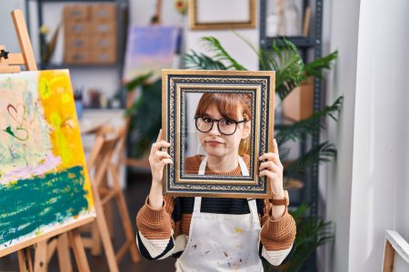 Photo for Young beautiful artist woman with face inside empty vintage frame clueless and confused expression. doubt concept. - Royalty Free Image