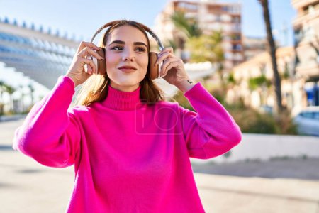 Téléchargez les photos : Jeune femme souriante à l'écoute de musique au parc - en image libre de droit