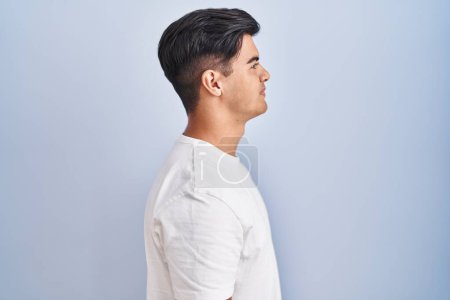 Photo for Hispanic man standing over blue background looking to side, relax profile pose with natural face and confident smile. - Royalty Free Image