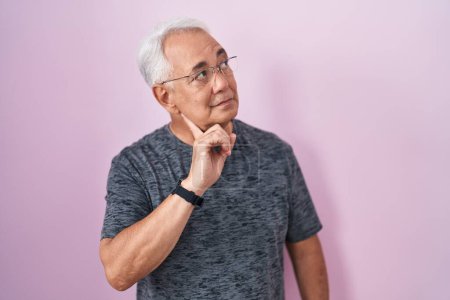 Photo for Middle age man with grey hair standing over pink background with hand on chin thinking about question, pensive expression. smiling with thoughtful face. doubt concept. - Royalty Free Image