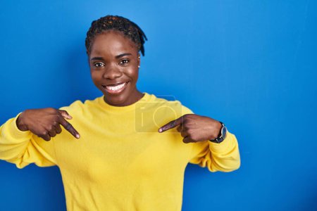 Foto de Beautiful black woman standing over blue background looking confident with smile on face, pointing oneself with fingers proud and happy. - Imagen libre de derechos