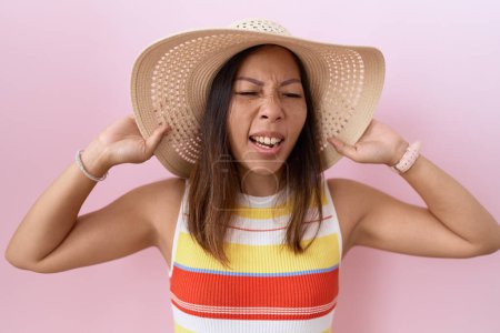 Foto de Mujer china de mediana edad con sombrero de verano sobre fondo rosa enojado y loco gritando frustrado y furioso, gritando con ira. rabia y concepto agresivo. - Imagen libre de derechos