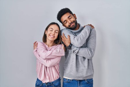 Photo for Young hispanic couple standing together hugging oneself happy and positive, smiling confident. self love and self care - Royalty Free Image