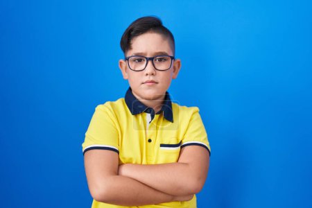 Photo for Young hispanic kid standing over blue background skeptic and nervous, disapproving expression on face with crossed arms. negative person. - Royalty Free Image