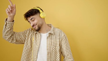 Téléchargez les photos : Jeune homme arabe écoutant de la musique danser sur fond jaune isolé - en image libre de droit