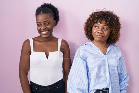 Téléchargez les photos : Deux femmes africaines debout sur fond rose souriant regardant vers le côté et regardant loin en pensant. - en image libre de droit