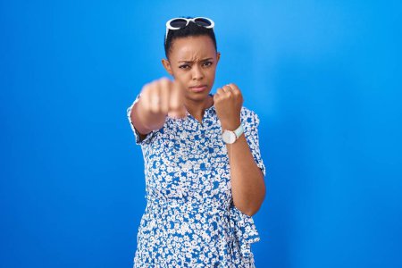 Téléchargez les photos : African american woman standing over blue background punching fist to fight, aggressive and angry attack, threat and violence - en image libre de droit