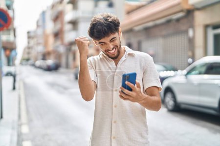Foto de Young arab man using smartphone with winner expression at street - Imagen libre de derechos