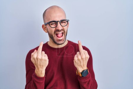 Téléchargez les photos : Young bald man with beard standing over white background wearing glasses showing middle finger doing fuck you bad expression, provocation and rude attitude. screaming excited - en image libre de droit