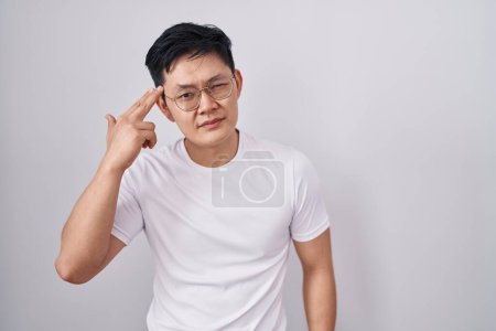 Téléchargez les photos : Jeune homme asiatique debout sur fond blanc tirant et se suicidant pointant la main et les doigts vers la tête comme un pistolet, geste de suicide. - en image libre de droit
