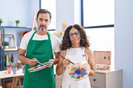 Photo for Middle age hispanic couple painting at art studio relaxed with serious expression on face. simple and natural looking at the camera. - Royalty Free Image